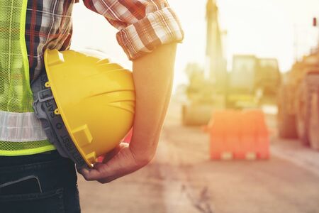 Engineer holding helmet at road construction site with machinery background,safety first conceptの写真素材