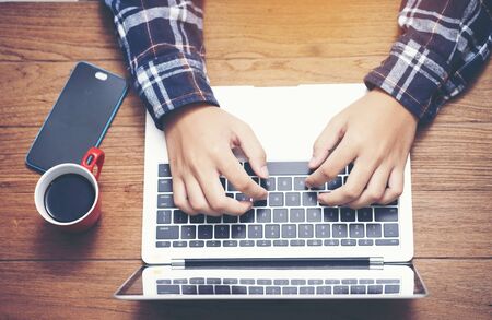 Businessman useing laptop with asmartphone and coffee on wooden table, top view from above