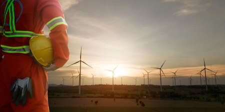 Engineer holding helmet with wind turbines plant for electric power production silhouette at sunset ,clean energy conceptの写真素材