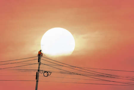 Electrician worker climbing electric power pole with sun backgroundの写真素材