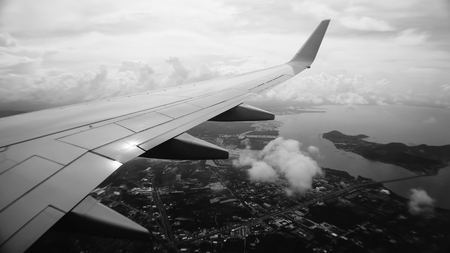 View from airplane window. Wing of an airplane flying above the clouds over tropical island in black...