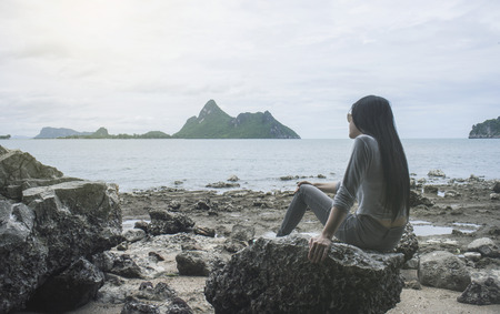 young asian woman sitting on a rock near the sea,looked to the sea,chill out of summer,rest time,light effect added,selective focus,filtered imageの写真素材