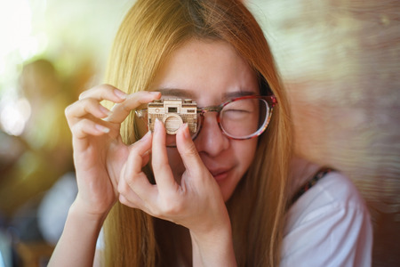 young asian woman raising a wooden model camera to front of the eye like to take a camera,play with...