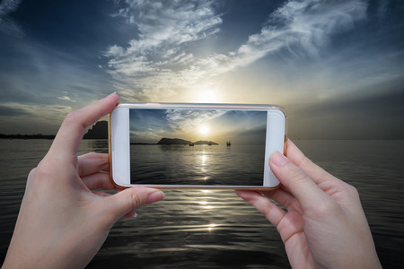 close up of woman hand holding a smartphone to take a photo of beautiful sunrise and cloud in a...