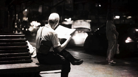 senior man read a newspaper among the dark of night beside the street,selective focus,abstract texture,vintage textured photoの写真素材