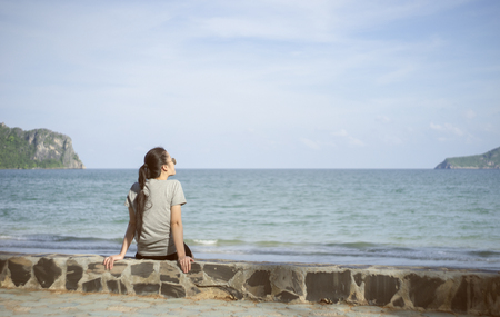 beautiful alone young asian woman at seashore near the beach.blurred sea and sky in background.selective focus.filtered imageの写真素材