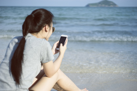 portrait of young asian woman using smart phone at beach.technology concept.blurred beach sea background.light effect added.の写真素材