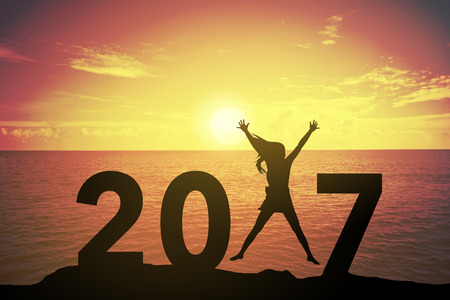 Silhouette young woman standing and raising up her hand about happy concept on at 2017 over a...