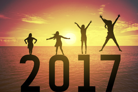 Silhouette young woman jumping and raising up her hand about happy concept on numbers 2017 over a beautiful sunset or sunrise at the sea, background for happy news years.success in 2017 yearsの写真素材