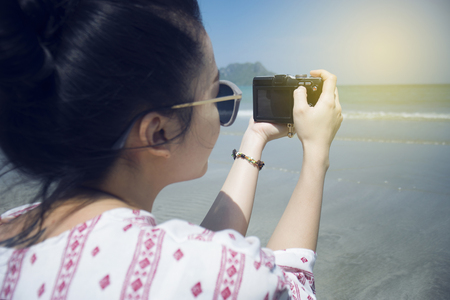 Asian teenager woman has take a relaxing on beautiful beach. Wearing sunglasses and holding a camera. Siam Smiling girl. rest time at the beach with big mountain. Filtered image. Selective focusの写真素材