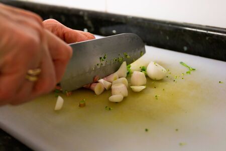hands with kitchen knife cutting vegetables on the white table in the kitchenの写真素材
