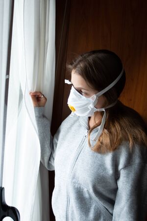 girl with mask looking out the window at homeの写真素材