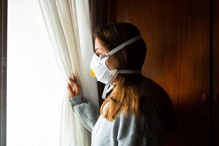girl with mask looking out the window at home