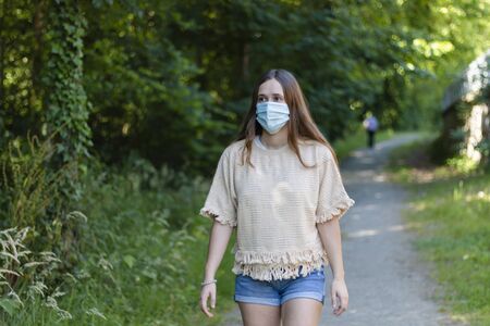 Woman walks through the garden with the mask on. Covid´19の写真素材