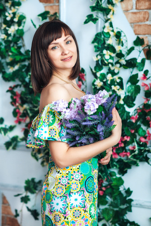 Beautiful brunette young woman in a bright dress holds flowers in handsの写真素材