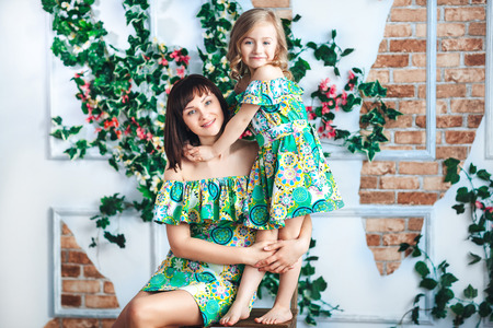 Happy mother and daughter in bright summer dresses hug and smile in roomの写真素材