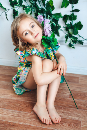 Little girl blonde sits on the floor with a flower in her hand in a room decorated with flowersの写真素材