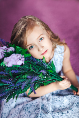 Portrait of a beautiful little blonde girl sitting on the floor with flowersの写真素材