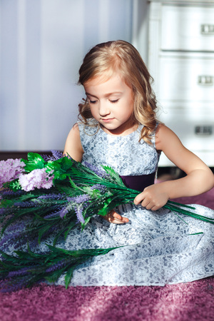 Little girl in a beautiful dress sits on the floor with flowers on her kneesの写真素材