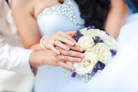Bride hand with ring and wedding bouquet of flowersの写真素材