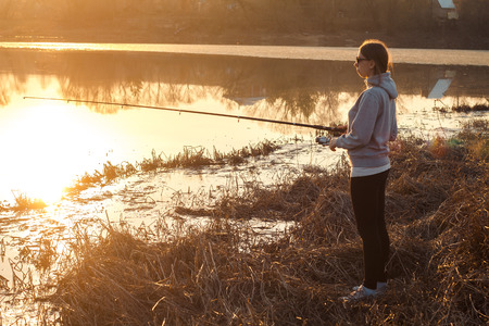 silhouette of a girl fishing at sunset near the lakeの写真素材