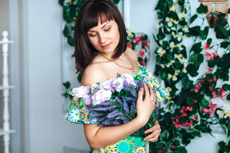 brunette young woman in a bright dress holds flowers in handsの写真素材