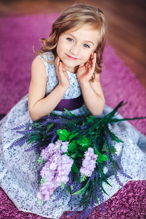 Little girl in a beautiful dress sits on the floor with flowers on her kneesの写真素材