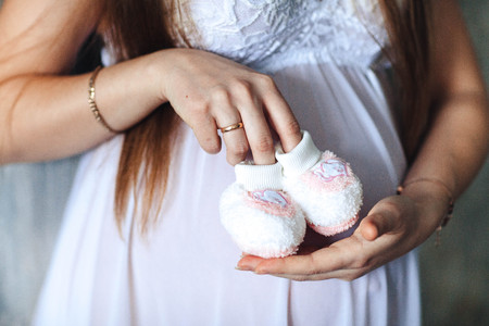 Healthy pregnancy. Newborn baby booties in parents hands. Pregnant woman belly