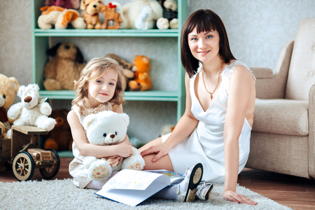 Happy mother with her daughter sitting in a room with a book in her handsの写真素材
