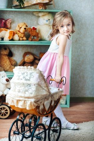 Happy little girl is playing with a stroller in the children's room, in doors at home or kindergartenの写真素材
