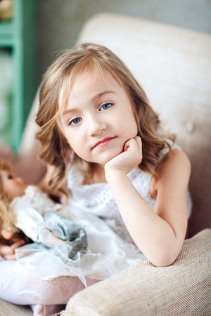 Cute blond girl in white dress sits in chairの写真素材