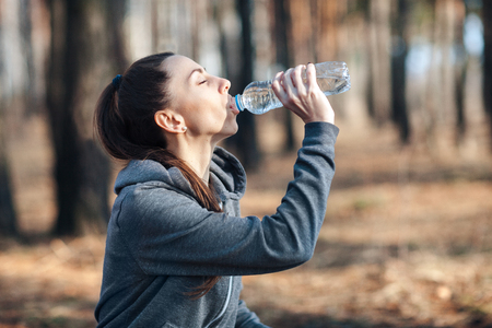 Close-up, young sports woman is drinking water after training in natureの写真素材