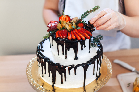 Female hand decorates a white cream cake with fruitの写真素材