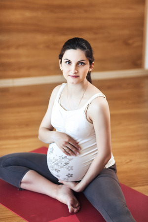 Portrait of a beautiful young pregnant woman sitting on yoga Matの写真素材