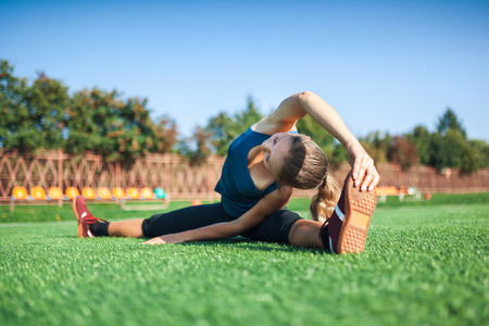 Young fitness girl doing stretching in the sunset . Football field