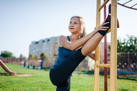A woman in sportswear doing warming-up exercises. City in sunny evening.Fit fitness woman doing...