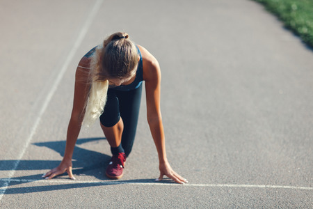 Portrait of young sporty woman in sport dress who are ready to run and stands on start on stadium trackの写真素材