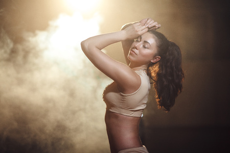 portrait of a sporty young woman with a tail in the top in the dark interior with lights and smokeの写真素材