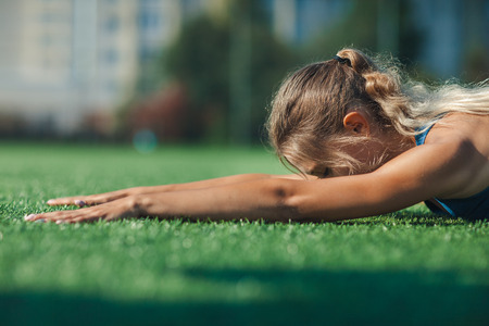 sports girl in a blue shirt and leggings doing gymnastics workout on a football field. Fitness, sport, health energy. Close upの写真素材