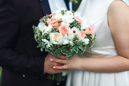 Hands of the newlyweds with a bouquet of the bride. Marriage concept.の写真素材