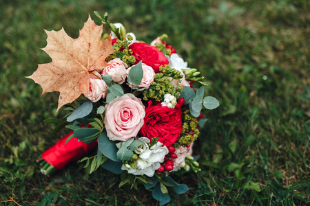 A bridal bouquet of a bride from white and red roses with red ribbon lies on a green grass