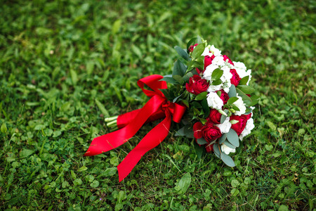 A bridal bouquet of a bride from white and red roses with red ribbon lies on a green grassの写真素材