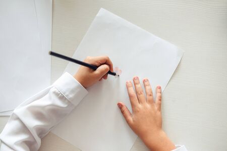 The child's hands are painted with colored pencils on a white sheet of paper on a wooden tableの写真素材