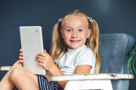 Technologies, people concept - young blondy girl sitting on a chair and watching the tablet or...