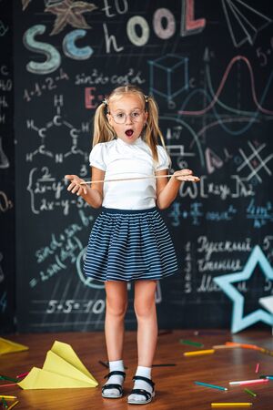 Little blonde girl with a surprised face with a ruler in her hands Pupil girl with big rulers against chalkboard with school formulas. back to school. Schoolgirl learning geometry. math lessonの写真素材