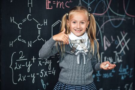 Cute girl in school uniform. Go to school for the first time. Girl indoors of the class room with blackboard on a background shows the thumb. Back to schoolの写真素材