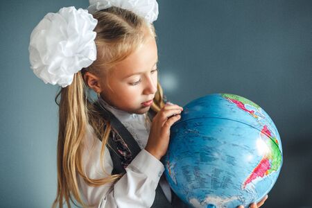 Portrait of a beautiful young schoolgirl girl exploring the globe through a magnifier. day of knowledge. beginning of the school year. studying geography with globeの写真素材