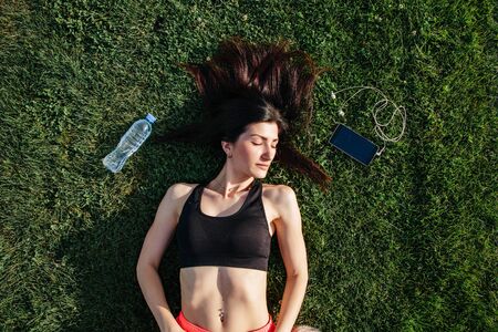 Portrait of a happy young fitness brunette woman lying on the football pitch after workout and...