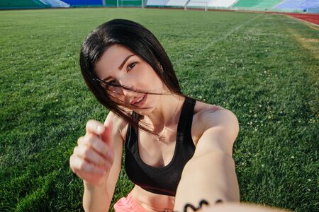 Young sporty brunette woman in girl in sports clothes doing selfie, smile face close up on grass....
