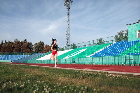 Young woman in pink shorts and tank to running during sunny morning on stadium track.の写真素材